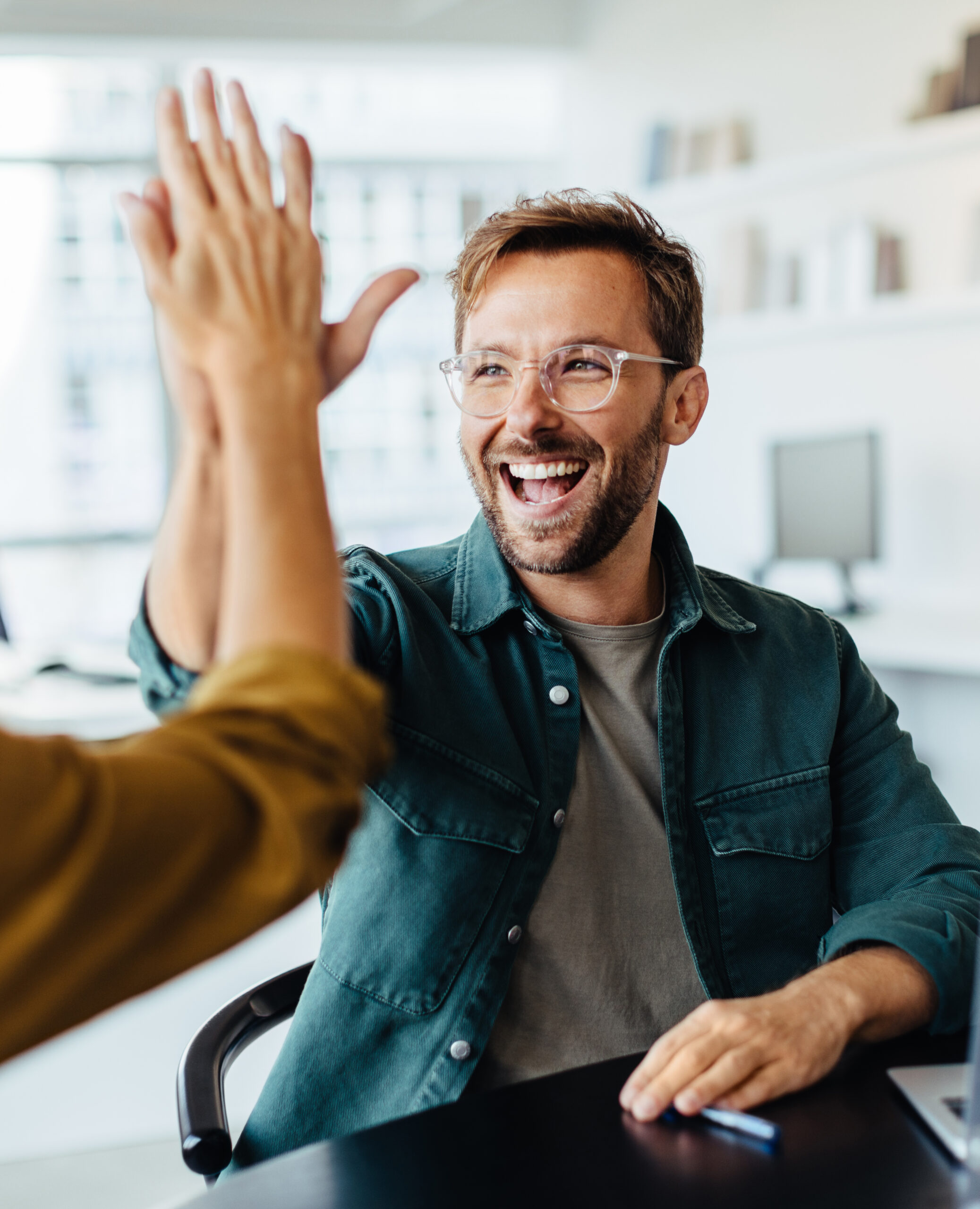 Successful business people giving each other a high five in a meeting. Two young business professionals celebrating teamwork in an office.